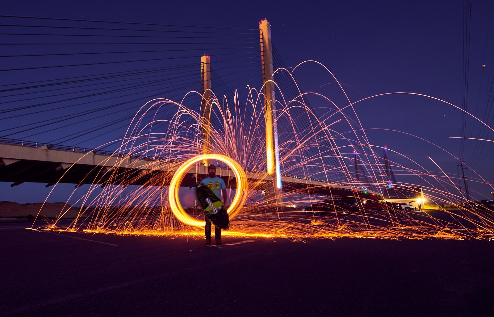 Man at the Indian River Inlet bridge at night with sparks flying and a skimboard