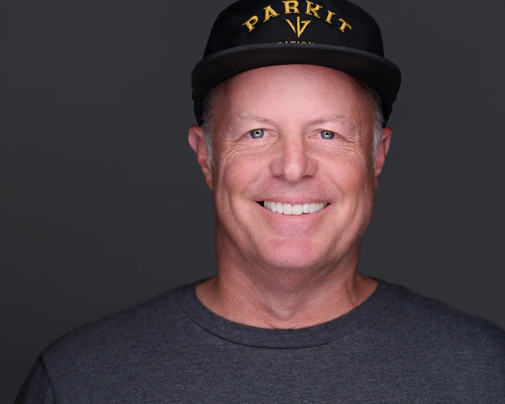 Man smiling wearing a black baseball style hat with gold writing
